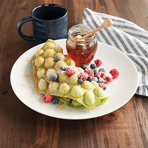 Egg waffle plated and sprinkled with sugar, berries, with a side of honey on a table. 